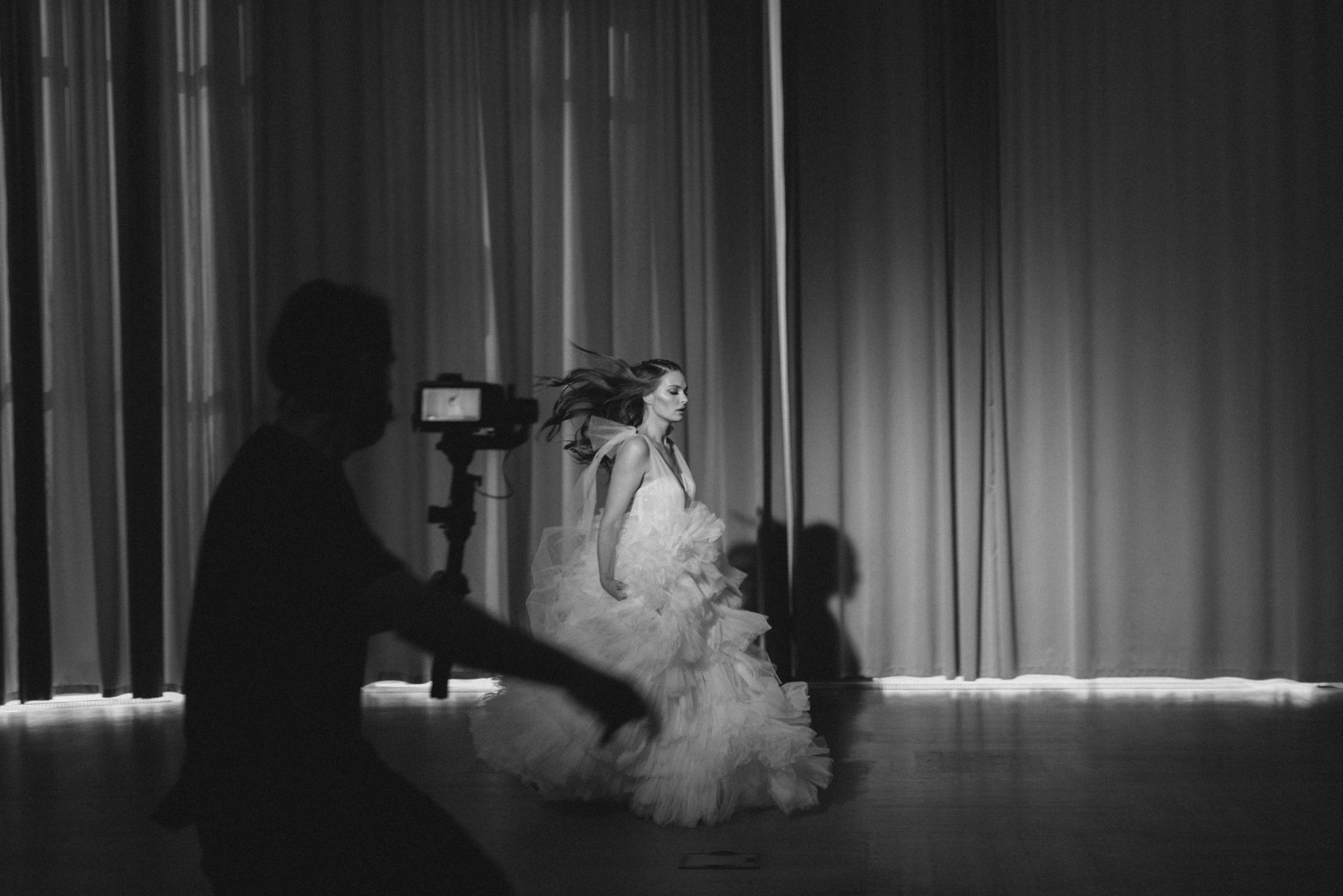 Grayscale photo of a woman running in wedding dress being caputred by a photographer.