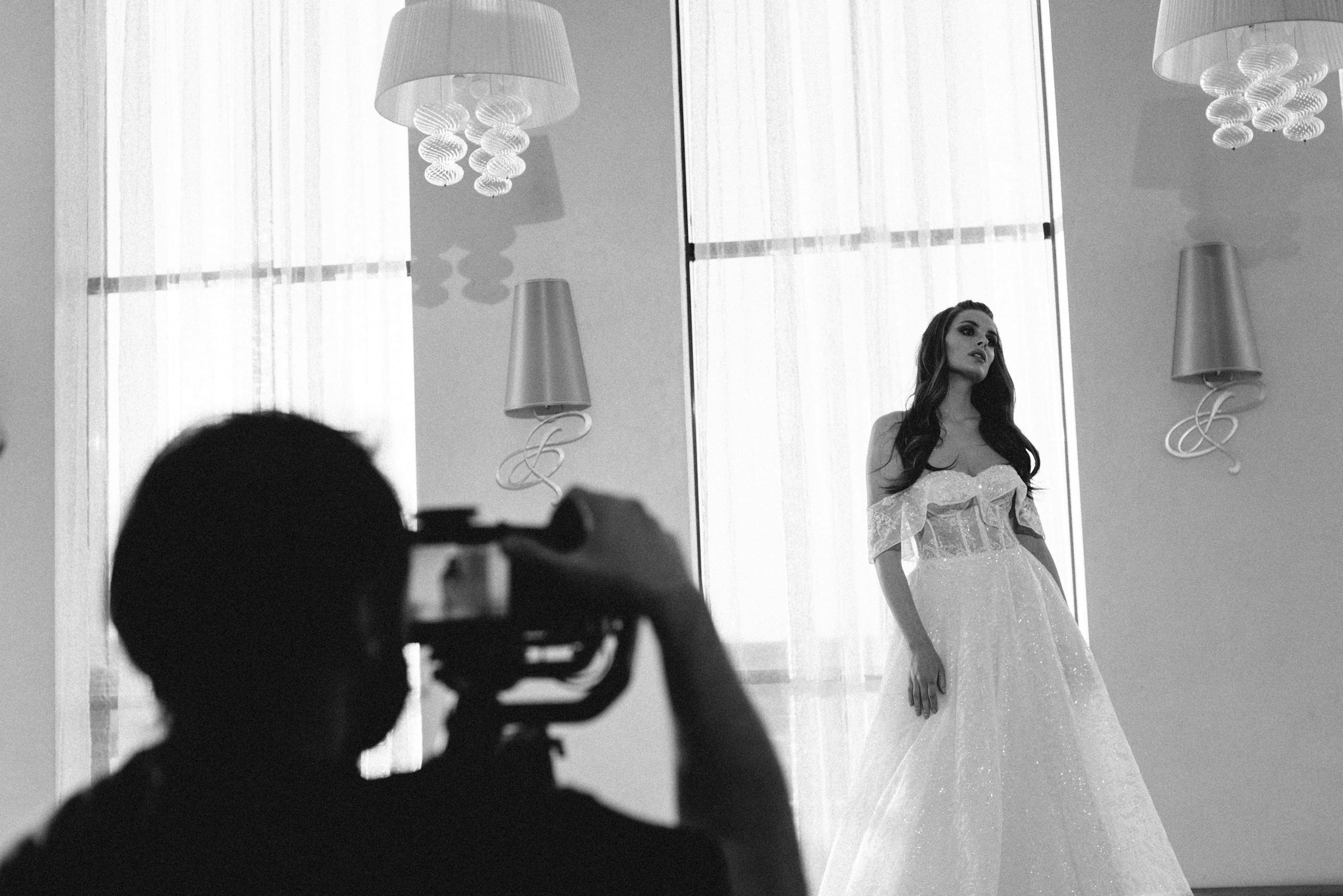 Grayscale photo of a posing woman in wedding dress being caputred by photographer.